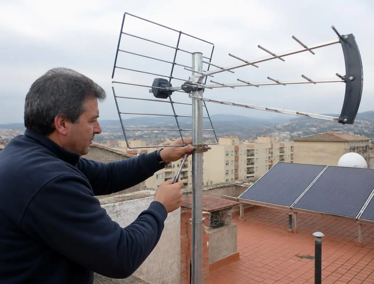 Antenista apretando el mástil de una antena UHF en la cubierta de un edificio de Esplugues