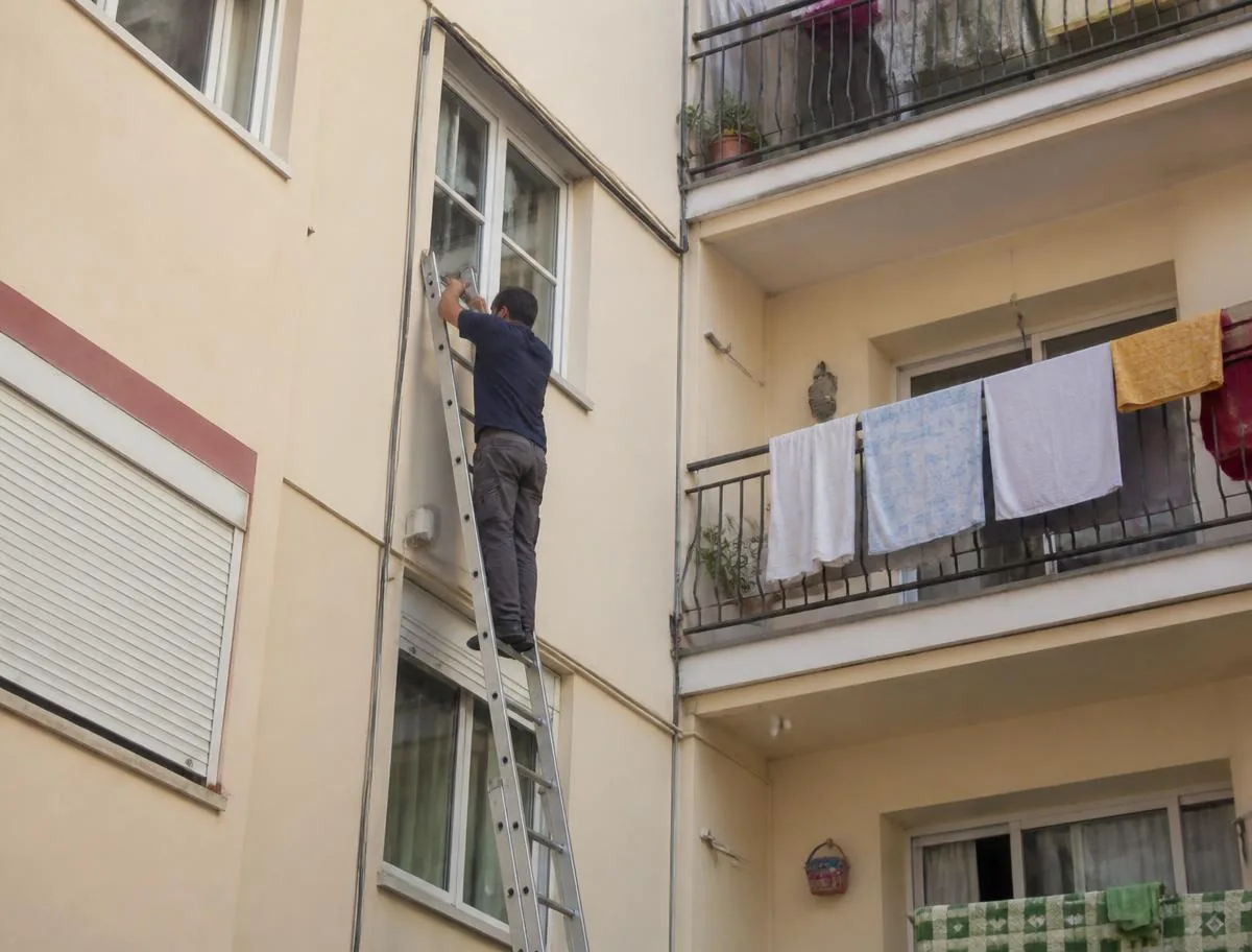 Antenista sobre escalera pasando cable coaxial por la fachada de un bloque en Sant Boi